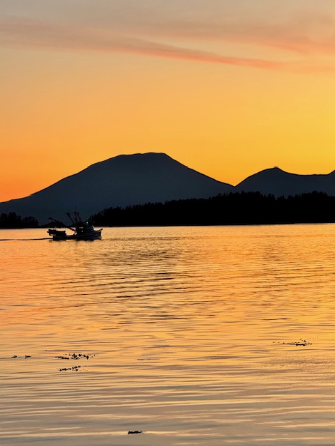 A fishing boat crossing golden water at sunset beneath Sitka's mountains